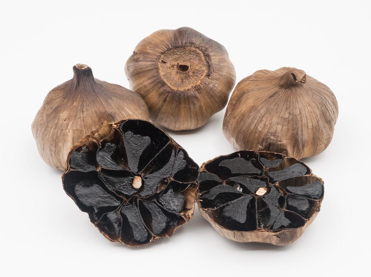 Cabeças de alho negro fermentado, algumas cortadas mostrando os dentes escuros