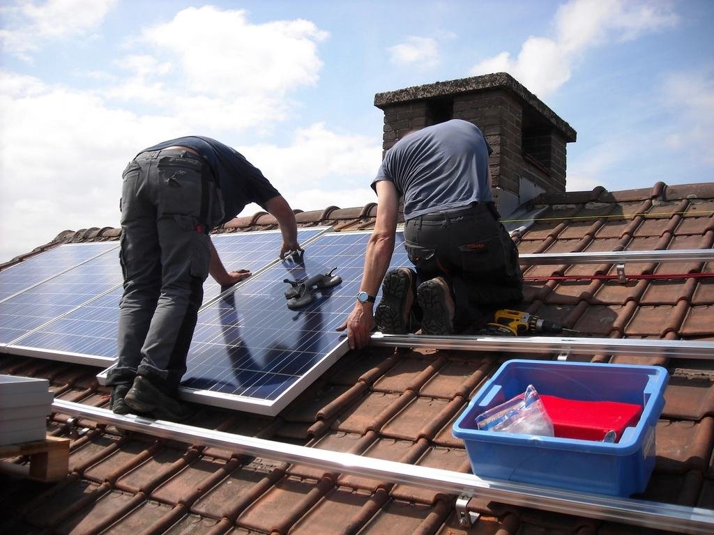Dois técnicos instalando painéis solares sobre um telhado de telhas