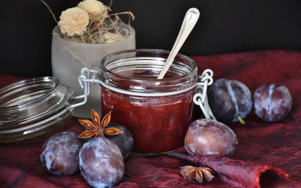 Pote de vidro com geleia de ameixa, ao lado de ameixas frescas e anis-estrelado